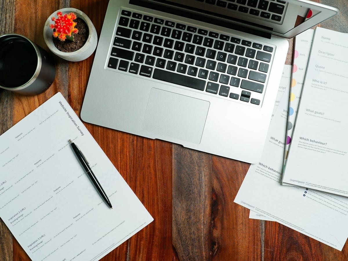 Laptop, printed forms and a pen on a wooden desk